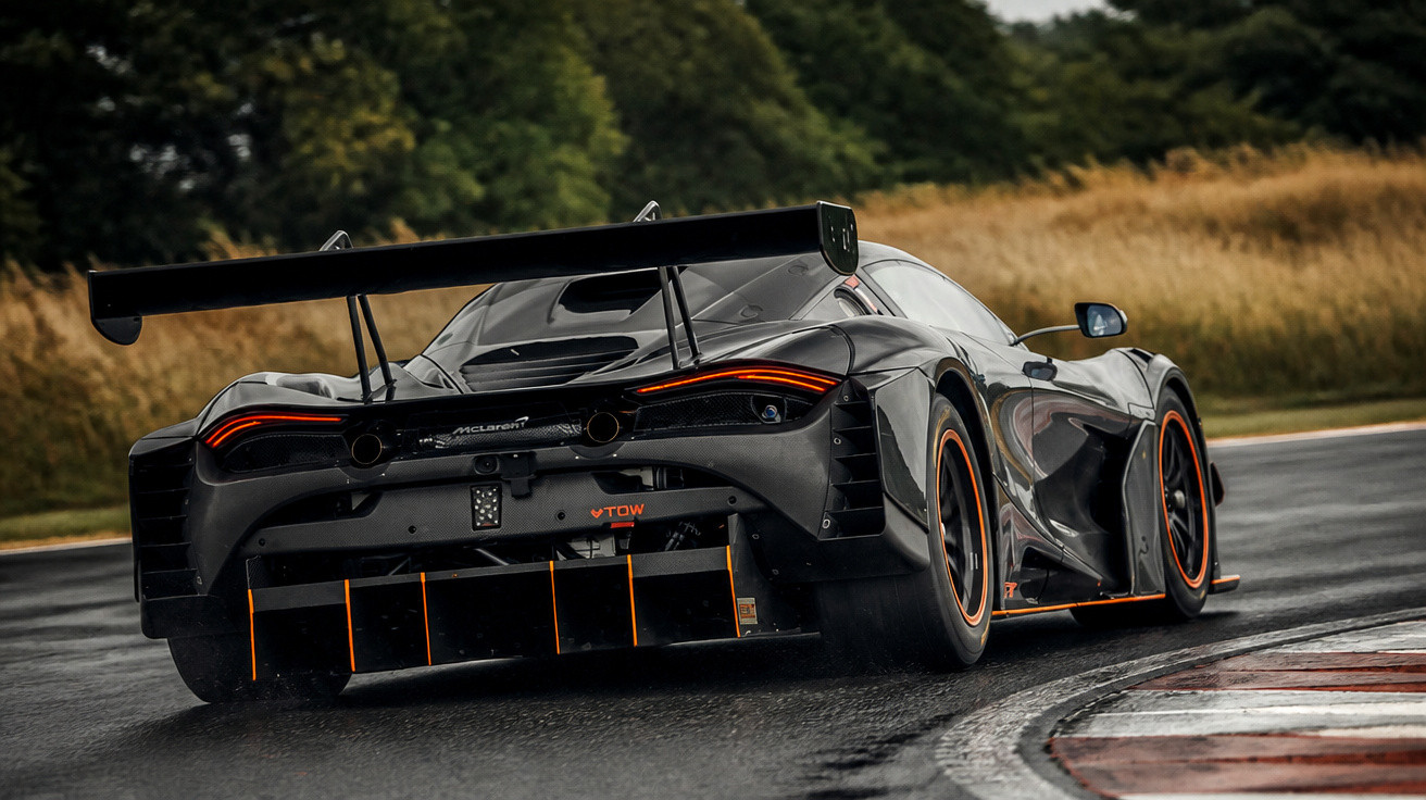 Carro esportivo McLaren preto com detalhes laranja em pista molhada durante curva em dia nublado.