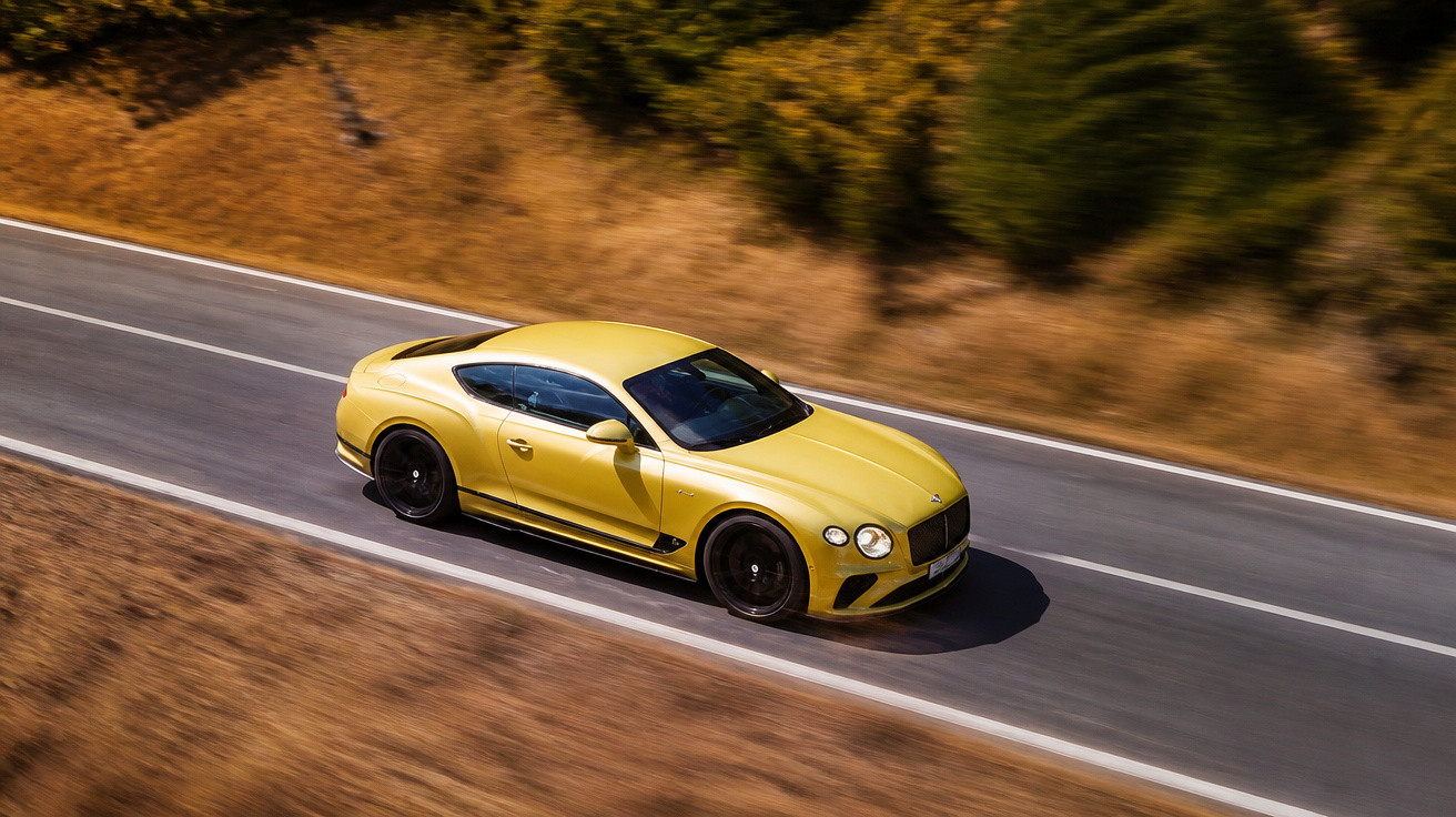Carro esportivo amarelo em alta velocidade numa estrada reta cercada por vegetação seca.