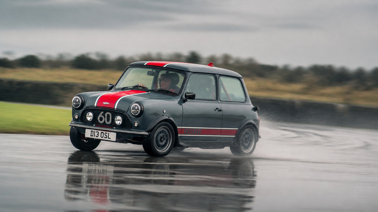 Carro Mini cinza com faixa vermelha dirigindo em pista molhada, gerando respingos d'água.