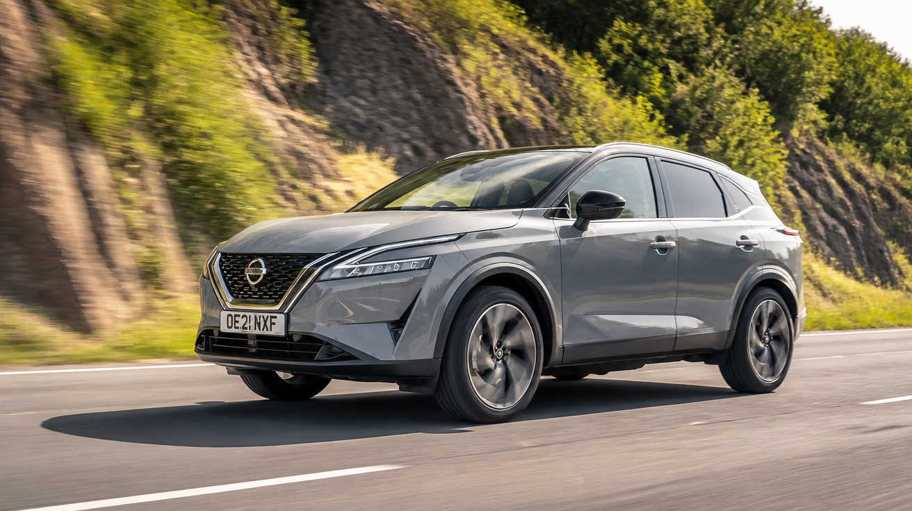 Carro SUV cinza da Nissan trafegando em uma estrada asfaltada ao lado de um talude com vegetação.