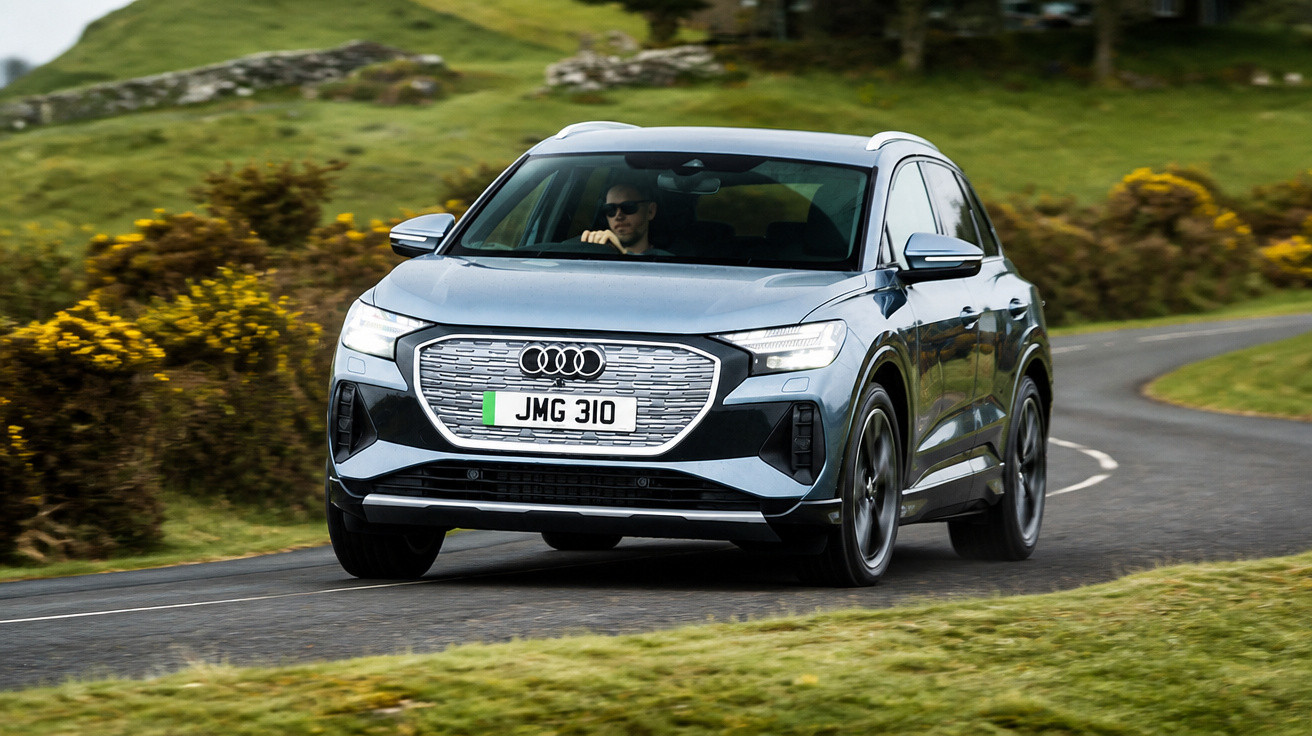 Audi SUV prata em estrada sinuosa com motorista usando óculos escuros em área verde.