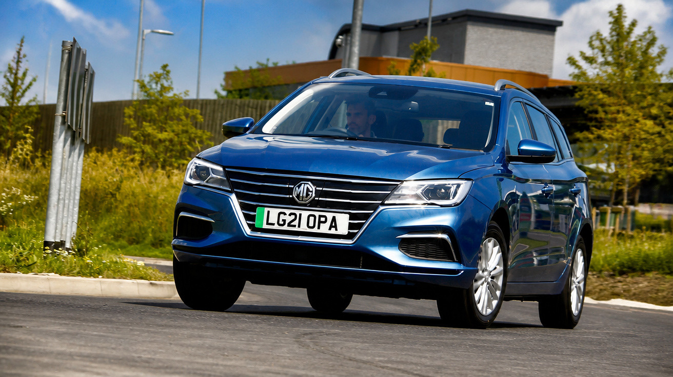 Carro azul MG modelo estate em curva numa estrada urbana com vegetação ao fundo.