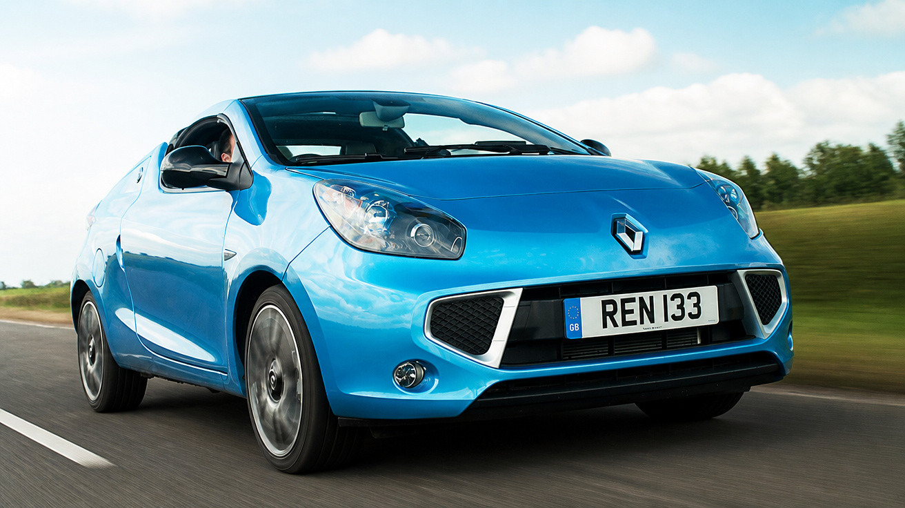 Carro azul Renault em movimento em estrada com céu azul e nuvens ao fundo.