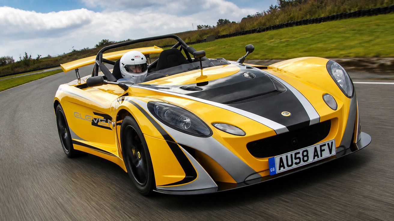 Carro esportivo amarelo com faixas pretas e prata em pista, motorista de capacete branco pilotando.
