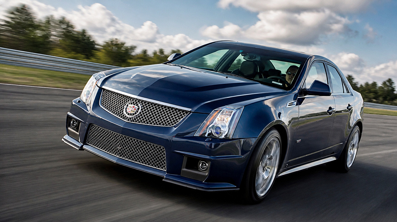 Carro esportivo Cadillac preto em alta velocidade em pista sobre asfalto com céu nublado ao fundo.
