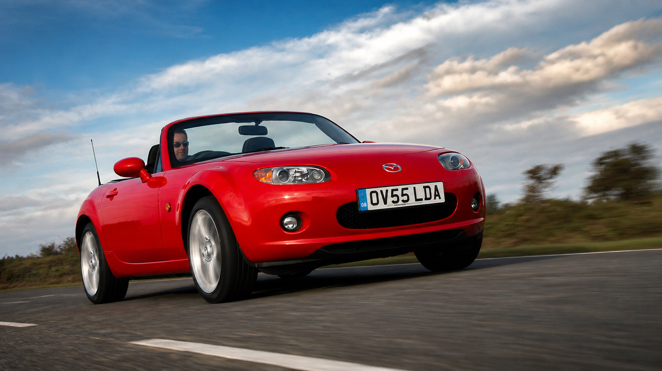 Carro conversível esportivo vermelho dirigindo em estrada sob céu azul com nuvens.