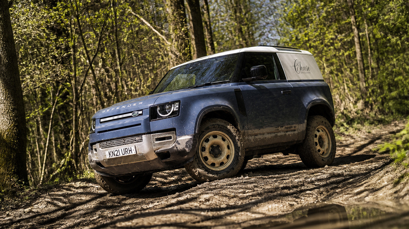 Carro azul Land Rover Defender estacionado em estrada de terra em floresta com folhas verdes.