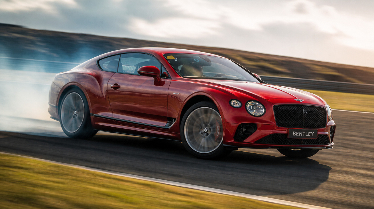 Carro esportivo Bentley vermelho fazendo curva rápida com fumaça saindo dos pneus em pista asfaltada.