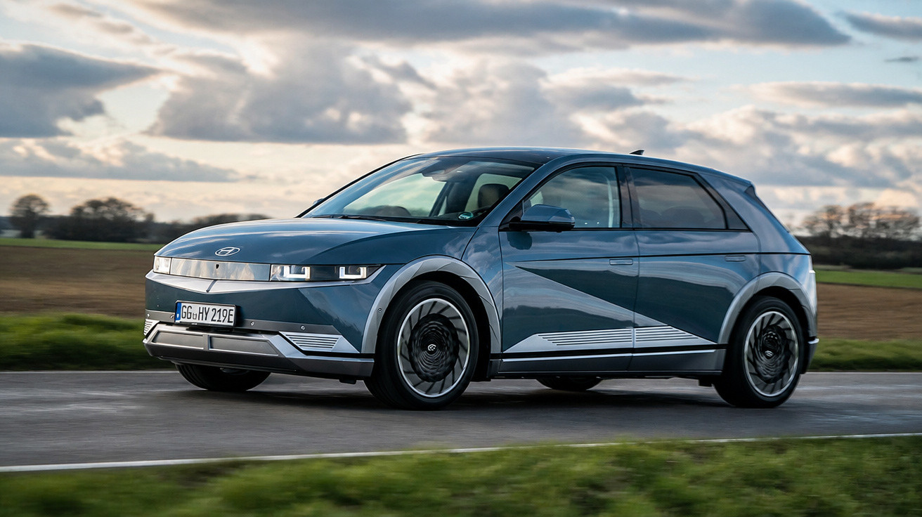 Carro elétrico Hyundai Ioniq 5 cinza em estrada reta com céu nublado e campo ao fundo.