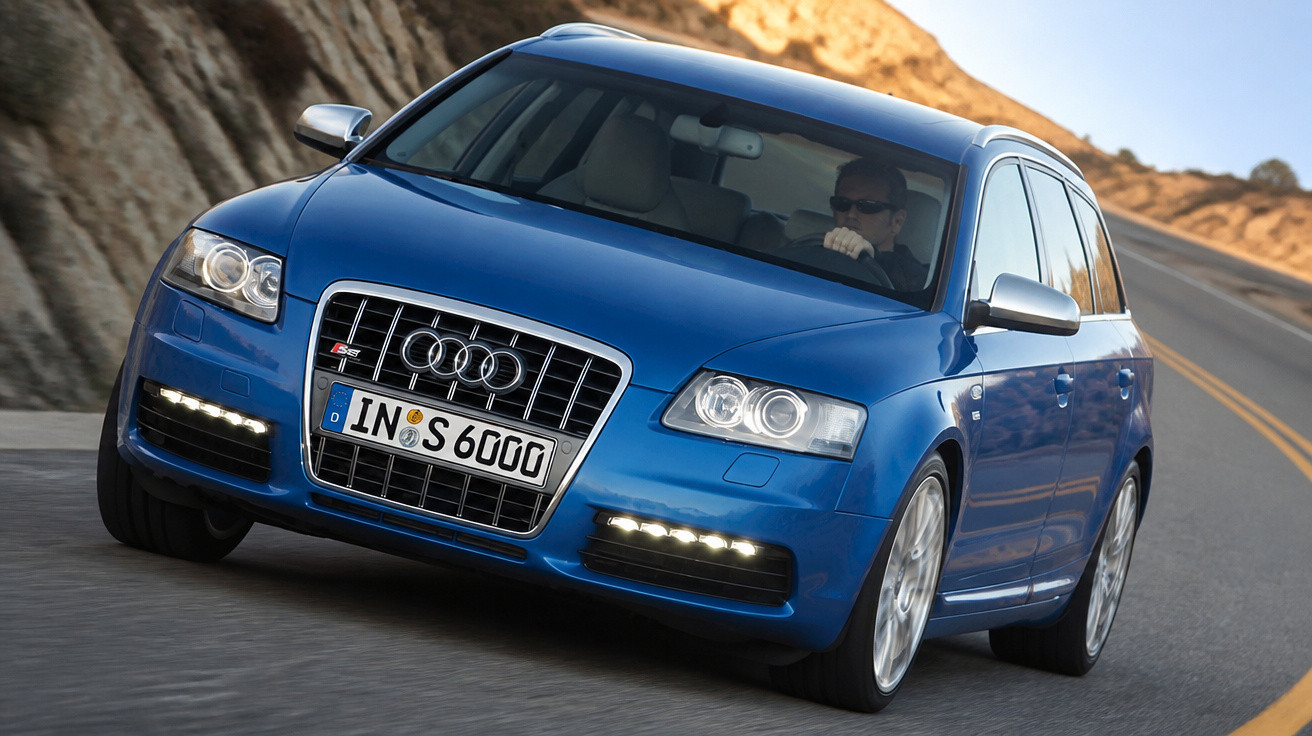 Carro Audi S3 azul em uma curva de estrada sinuosa, com motorista usando óculos escuros.