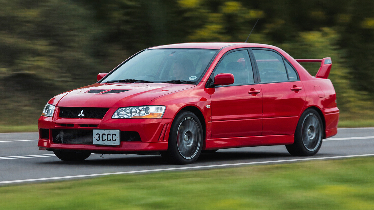 Carro esportivo vermelho Mitsubishi Evo em alta velocidade em estrada asfaltada com vegetação ao fundo.