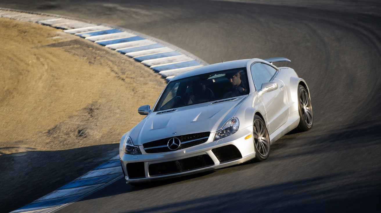 Carro esportivo Mercedes-Benz prata fazendo curva em pista de corrida asfaltada com borda pintada azul e branca.