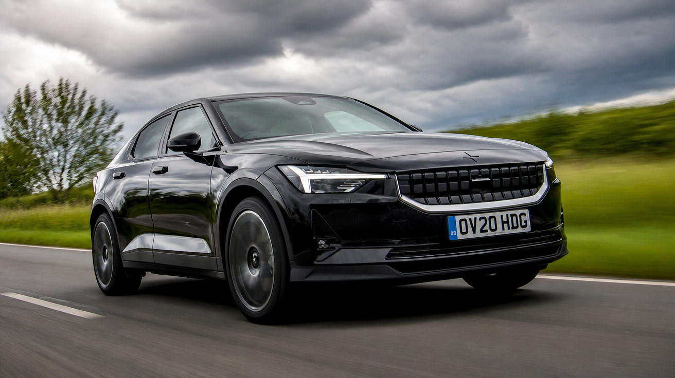 Carro elétrico preto Polestar 2 em movimento em estrada com céu nublado e vegetação ao fundo.