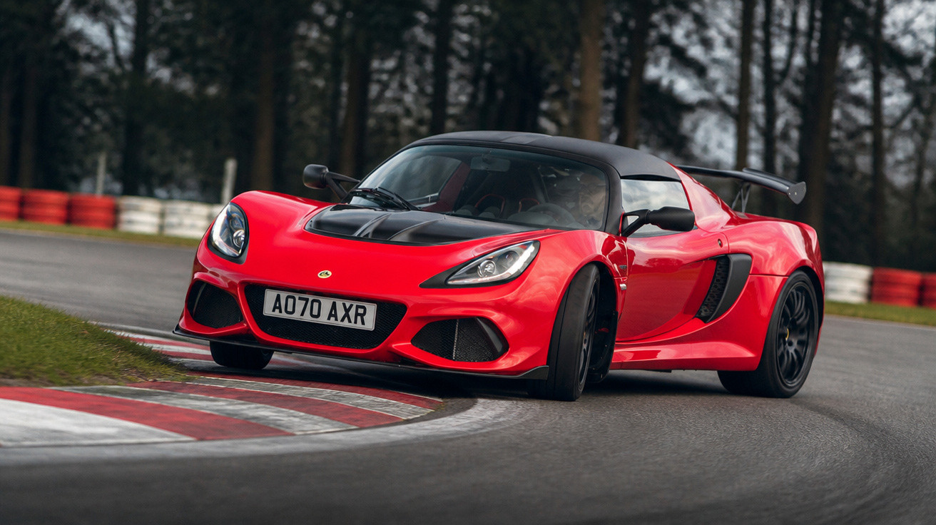 Carro esportivo vermelho com detalhes pretos fazendo curva em pista de corrida cercada por árvores.