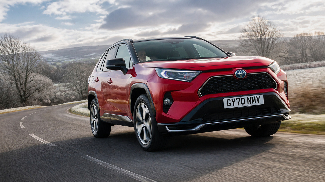 Carro SUV vermelho Toyota RAV4 em estrada sinuosa com céu nublado e árvores ao fundo.