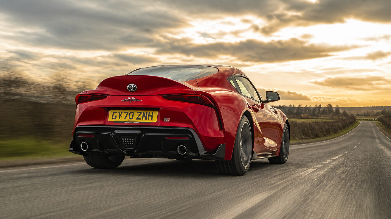 Carro esportivo vermelho Toyota GT86 dirigindo em estrada aberta sob céu nublado ao entardecer.