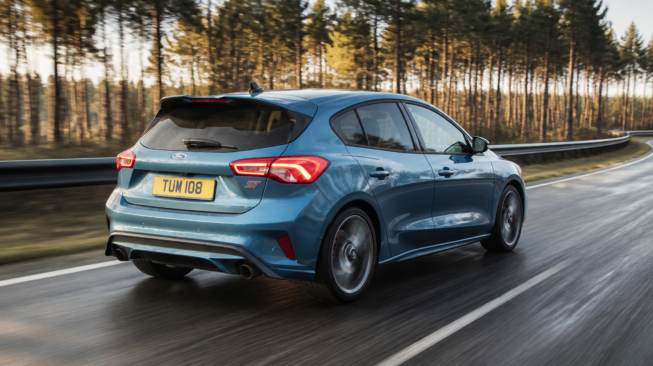 Carro azul Ford hatchback modelo ST em estrada molhada com árvores ao fundo em dia claro.