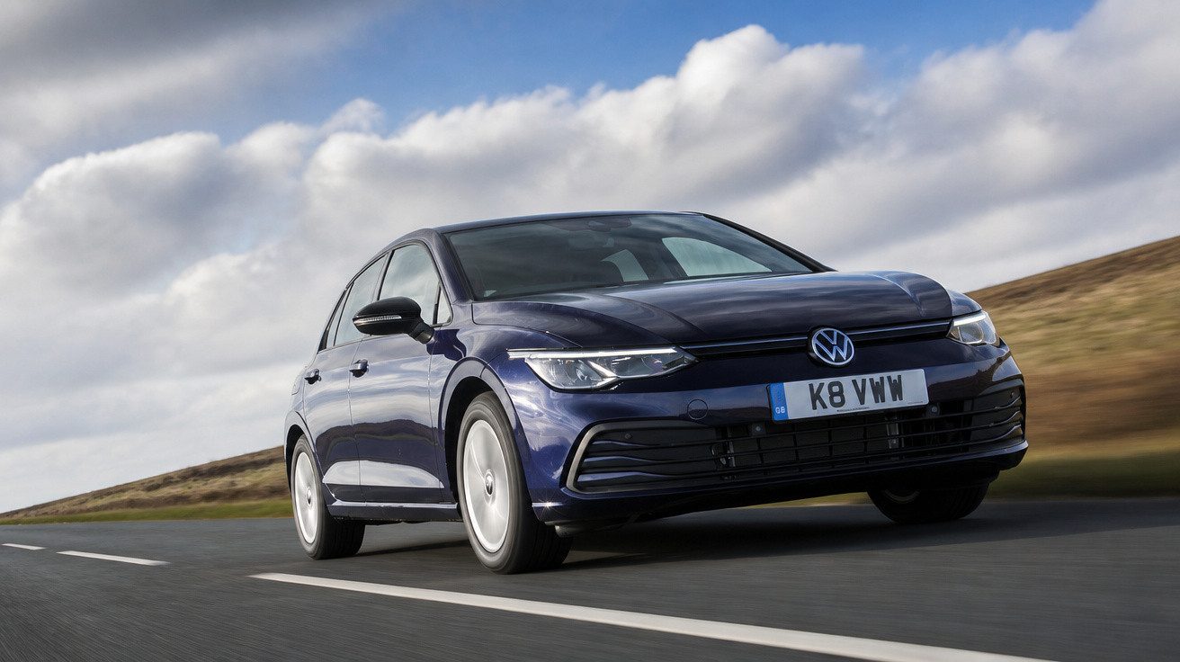 Carro Volkswagen Golf azul escuro em uma estrada sob céu nublado, com foco frontal.