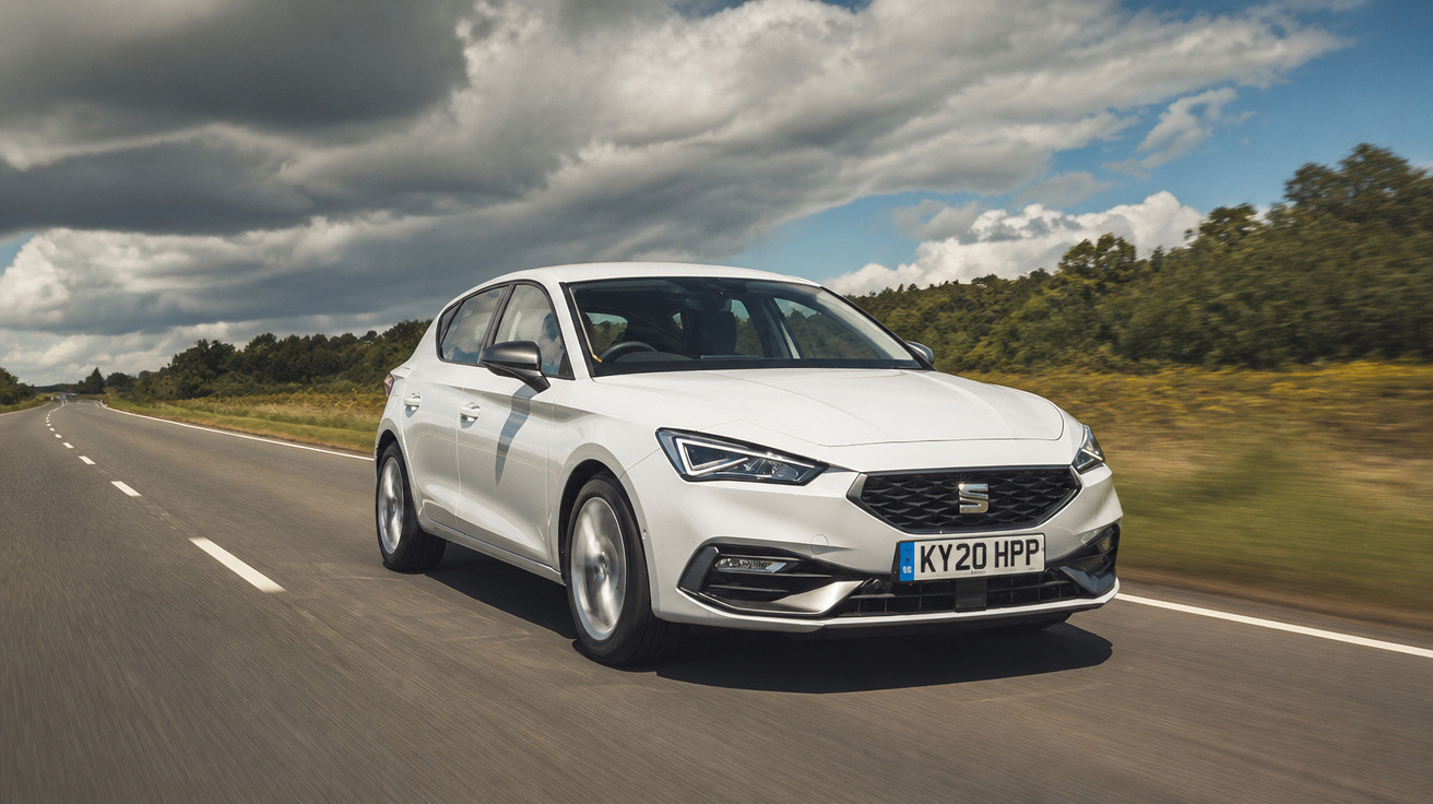 Carro branco modelo Seat Hatch hatchback dirigindo em estrada com céu parcialmente nublado e vegetação ao lado.