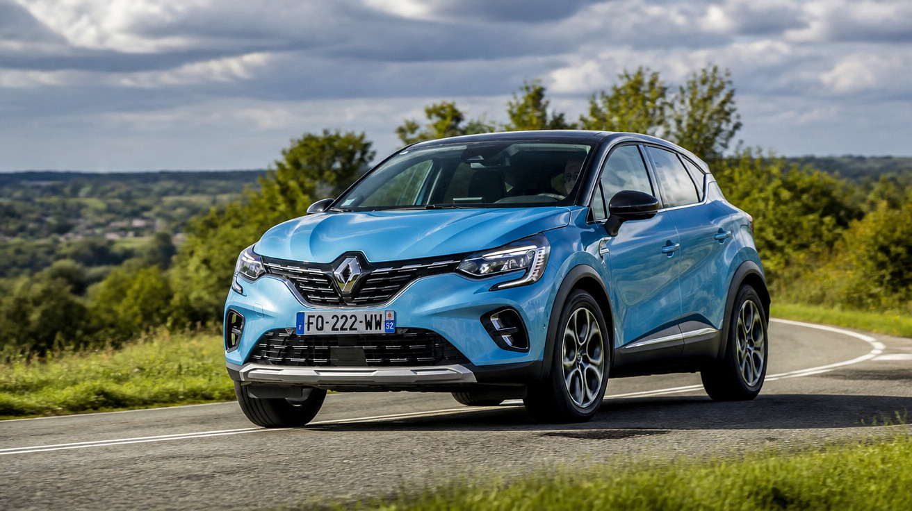Carro SUV azul da Renault circulando em estrada asfaltada com vegetação ao fundo em dia nublado.