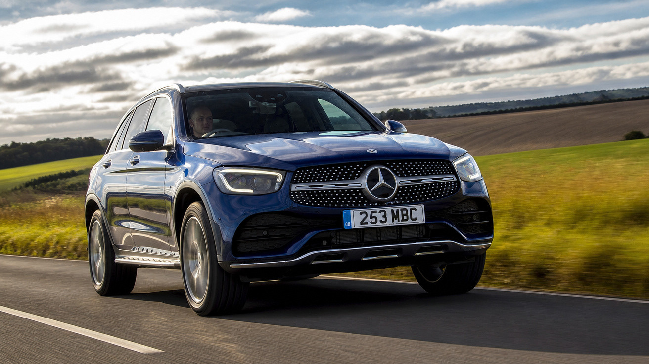 Carro SUV Mercedes-Benz azul em movimento em estrada cercada por campo e céu nublado.