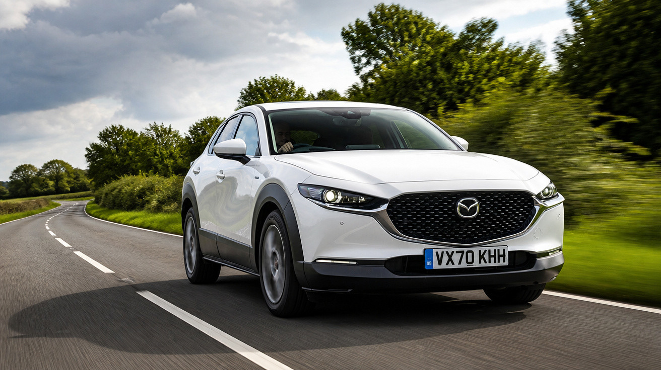 Carro branco Mazda CX-30 em estrada sinuosa cercada por vegetação e céu nublado.