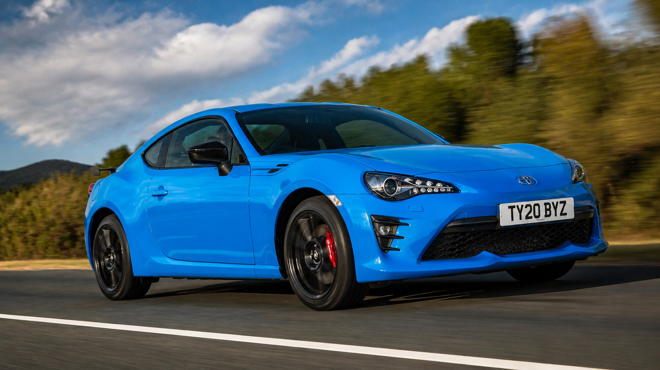 Carro esportivo azul Toyota em movimento em estrada com árvores ao fundo e céu parcialmente nublado.