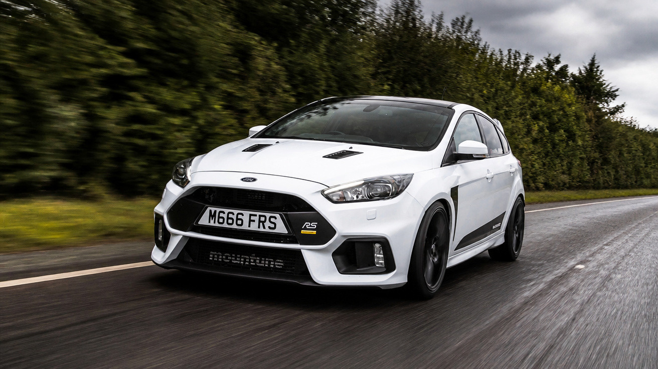 Carro esportivo branco Ford Focus RS em estrada molhada com árvores ao fundo em dia nublado.