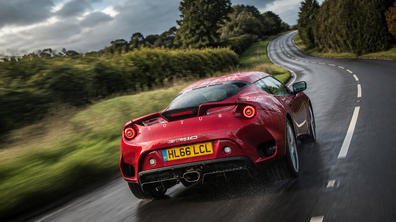 Carro esportivo vermelho Lotus GT410 dirigindo em estrada molhada cercada por árvores e arbustos.