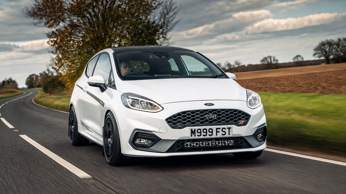 Carro esportivo branco Ford Fiesta ST dirigindo em estrada rural com céu nublado ao fundo.