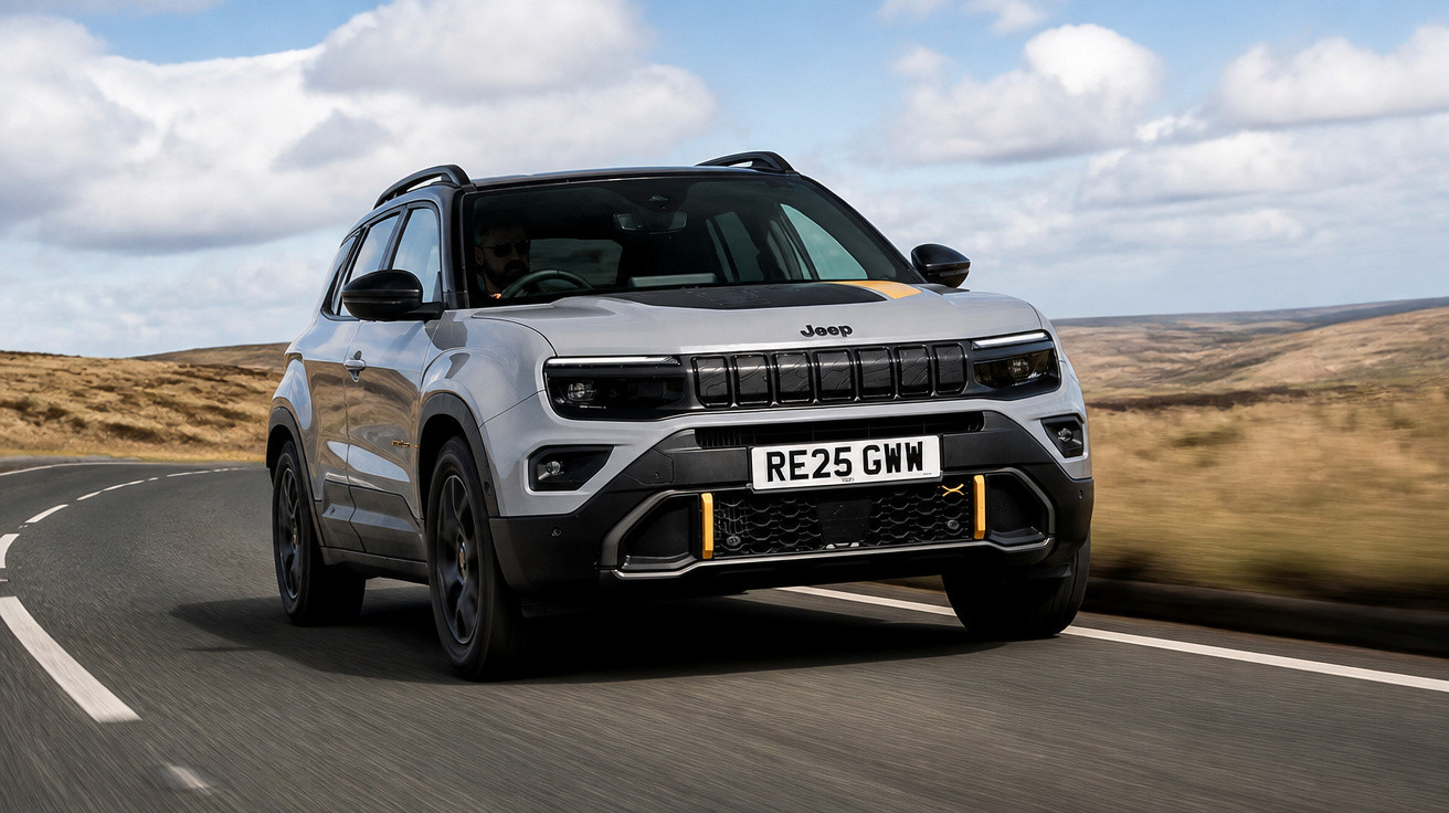 Carro Jeep SUV cinza dirigindo em estrada sinuosa com céu azul e nuvens ao fundo.