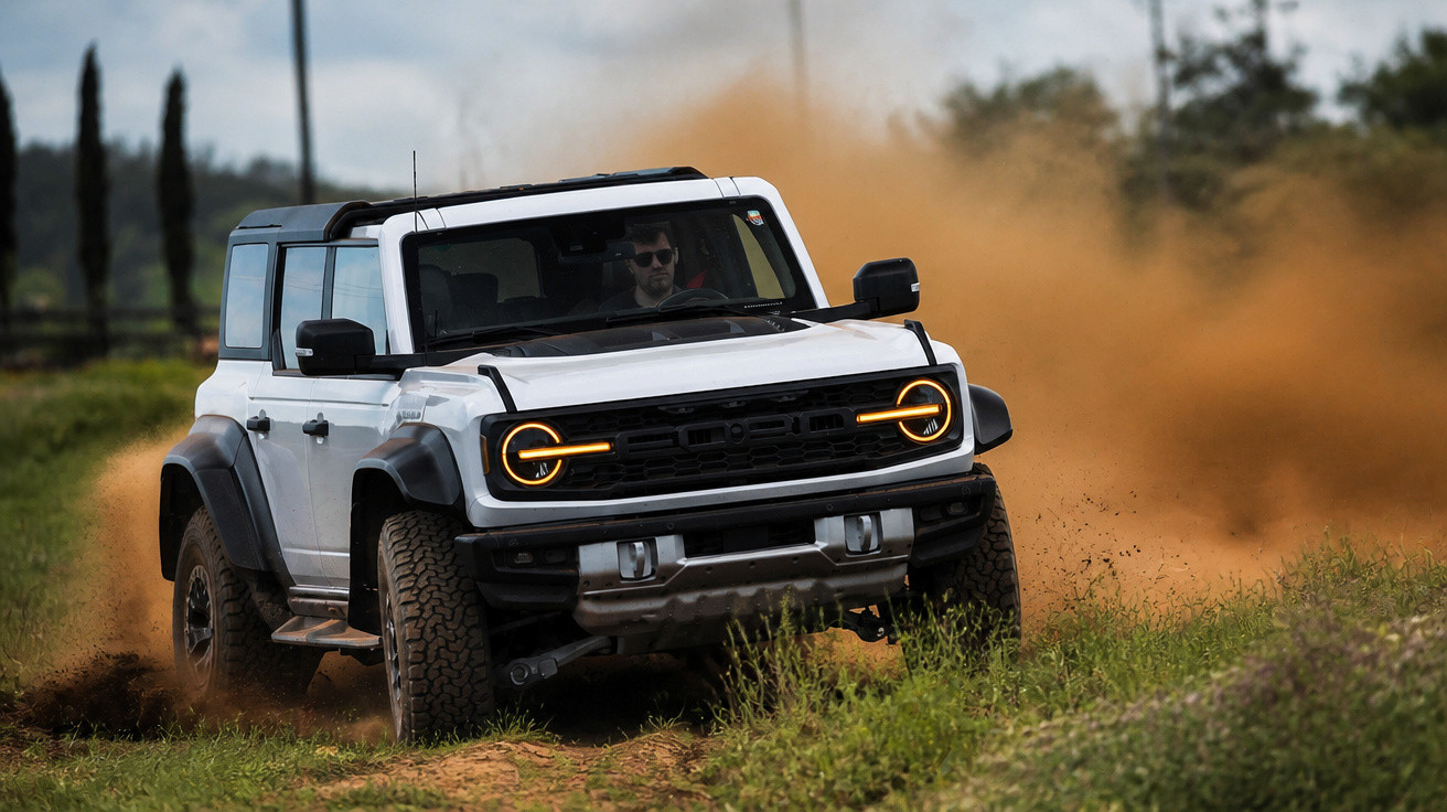 Carro SUV branco off-road em alta velocidade levantando poeira em trilha de terra com vegetação ao redor.