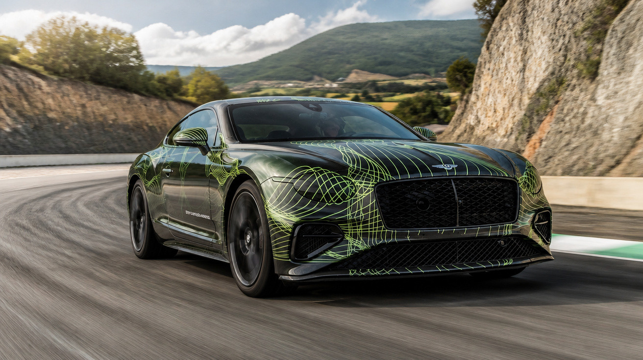 Carro esportivo preto com linhas verdes em alta velocidade em pista curva cercada por montanhas e vegetação.