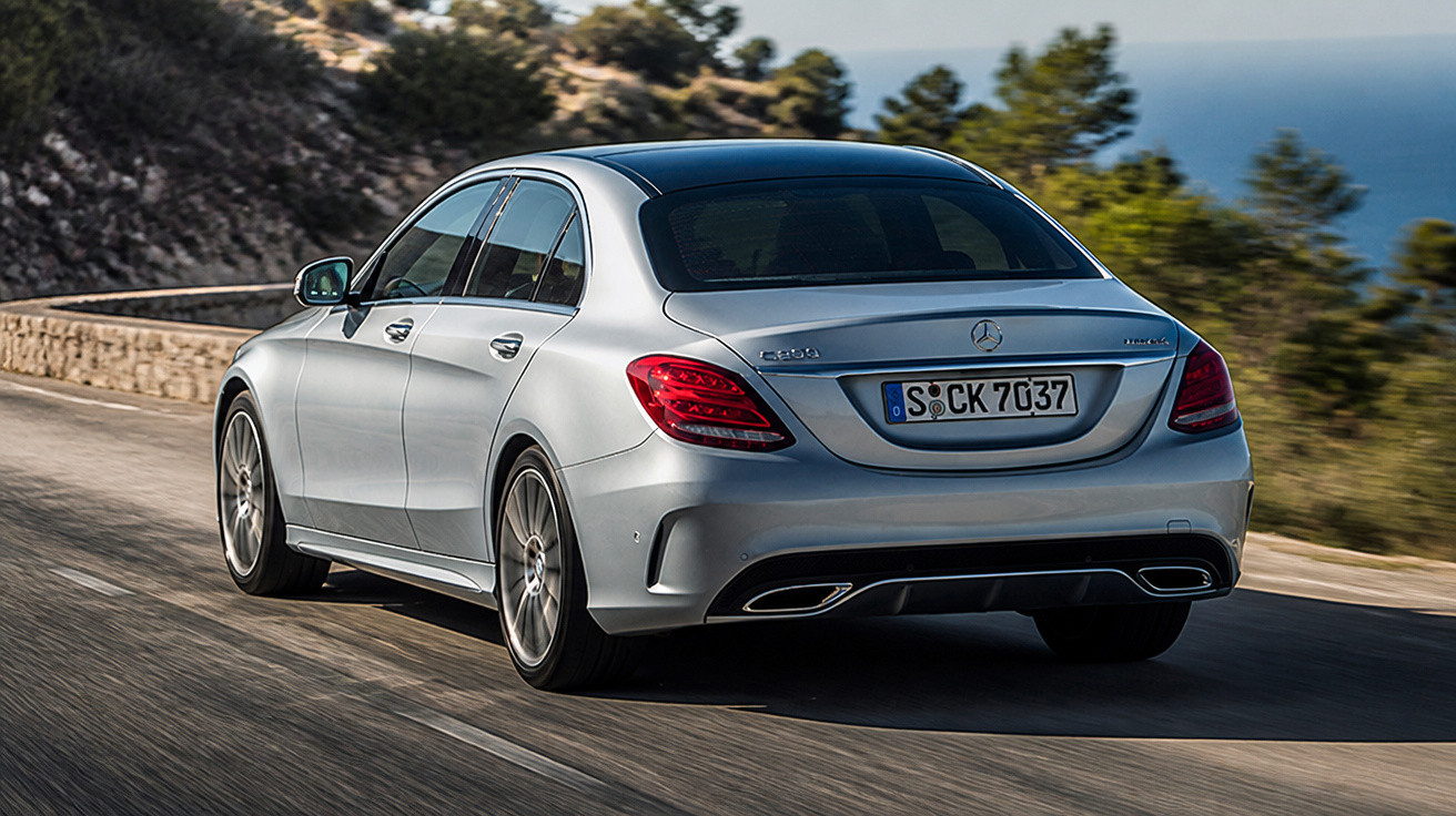 Carro prata Mercedes-Benz modelo C 300 rodando em estrada com paisagem de árvores e mar ao fundo.
