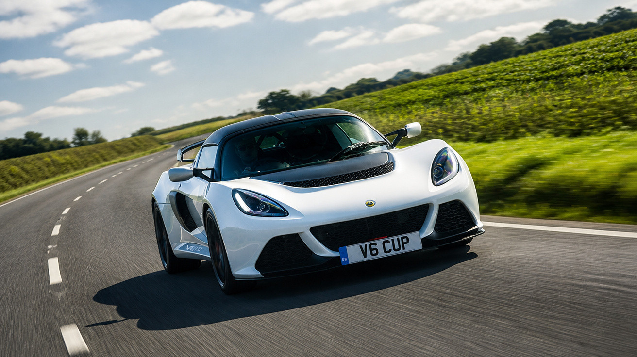 Carro esportivo branco Lotus V6 Cup trafegando em estrada curva ao lado de campo verde sob céu com nuvens.