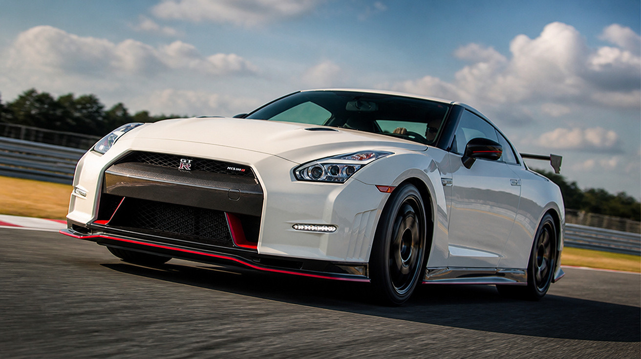 Carro esportivo branco Nissan GT-R Nismo em alta velocidade em pista de corrida sob céu nublado.