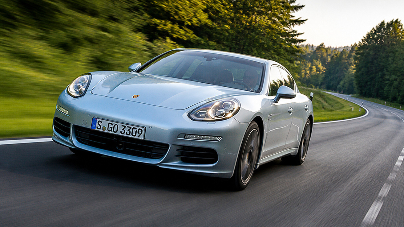 Carro esportivo prata Porsche Panamera em estrada sinuosa cercada por árvores verdes.