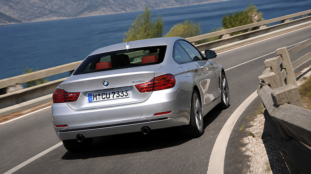 Carro prata BMW 435i dirigindo em estrada curva à beira de um lago com montanhas ao fundo.
