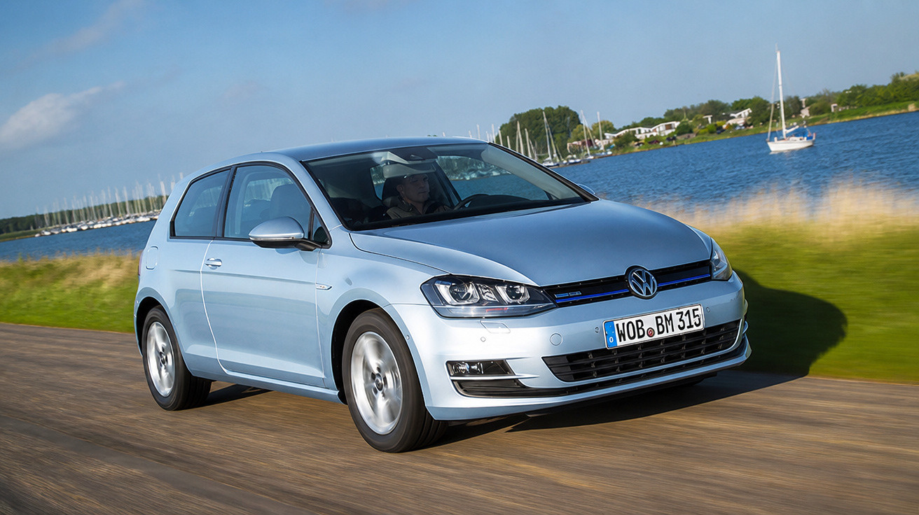 Carro Volkswagen Golf prata em movimento perto de um lago com barco e vegetação ao fundo.