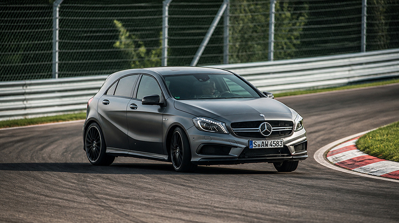 Carro esportivo Mercedes-Benz cinza fazendo curva em pista de corrida asfaltada com grades de proteção.