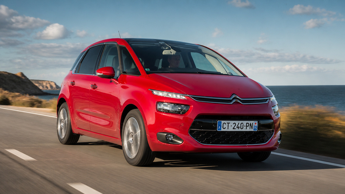 Carro Citroën vermelho em estrada costeira com céu azul e mar ao fundo.