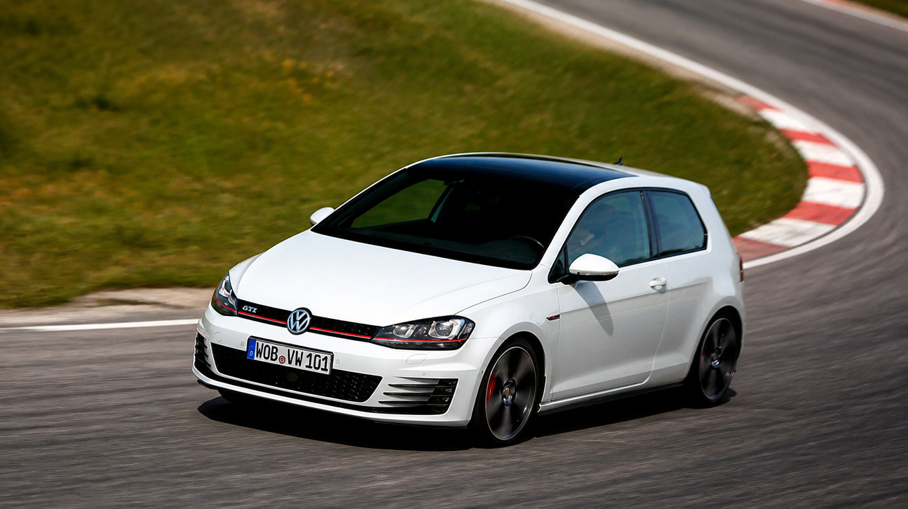 Carro Volkswagen GTI branco com teto preto fazendo curva em pista de corrida com gramado ao lado.
