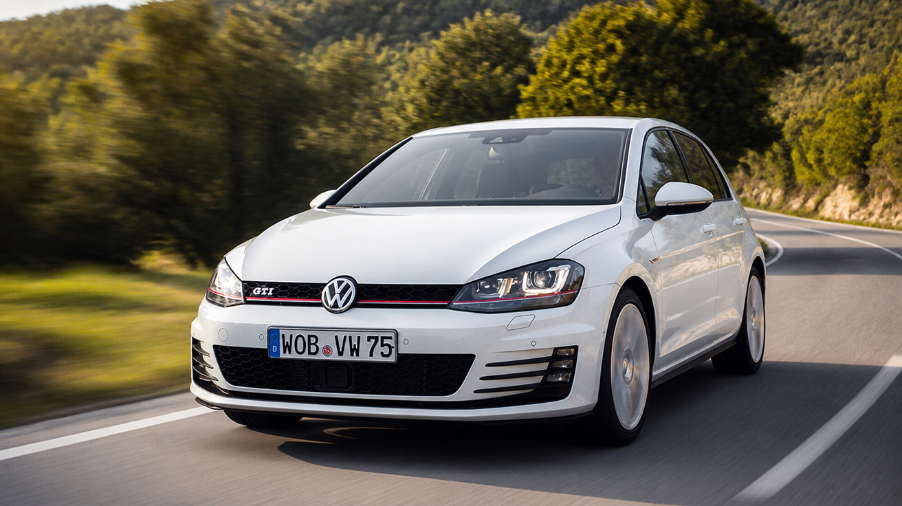 Carro branco Volkswagen Golf GTI em estrada cercada por árvores e vegetação.