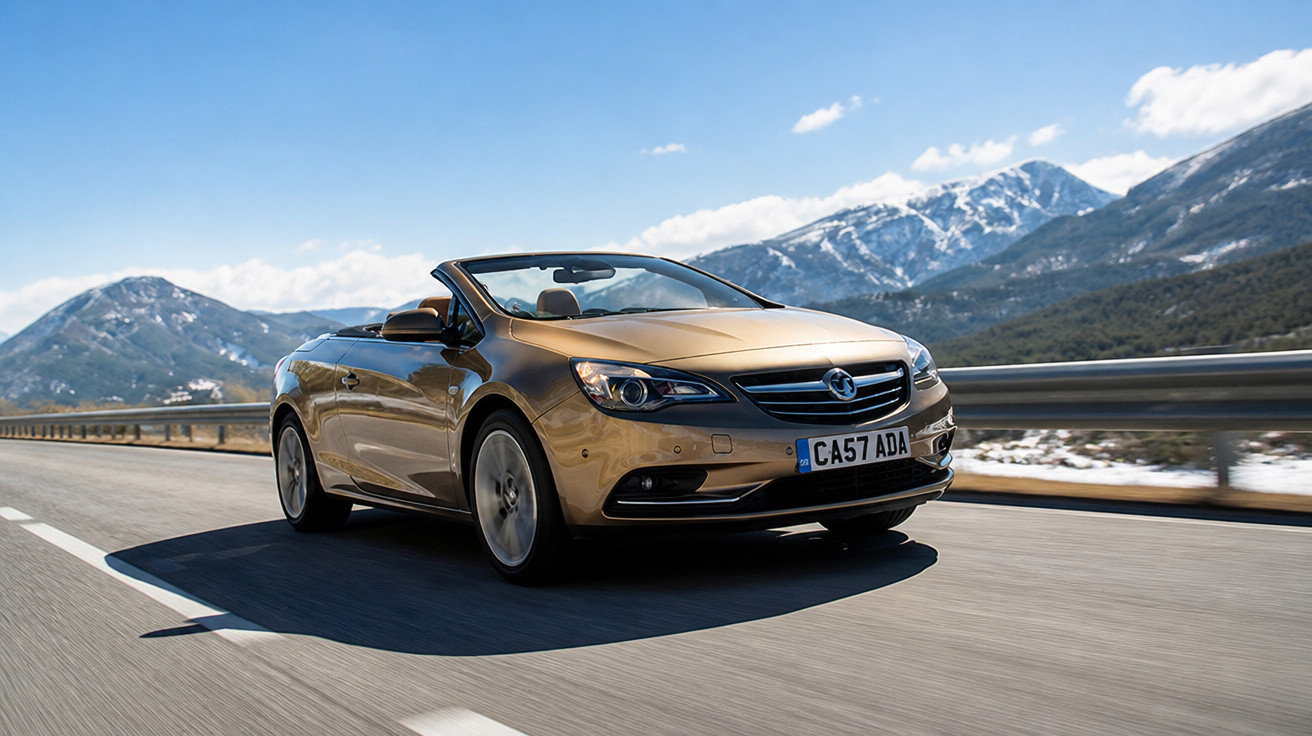 Carro conversível dourado em movimento em estrada com montanhas ao fundo em dia ensolarado.