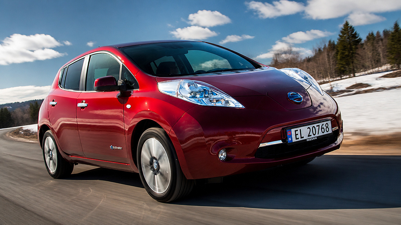 Carro elétrico Nissan Leaf vermelho em estrada sinuosa com paisagem de inverno ao fundo.