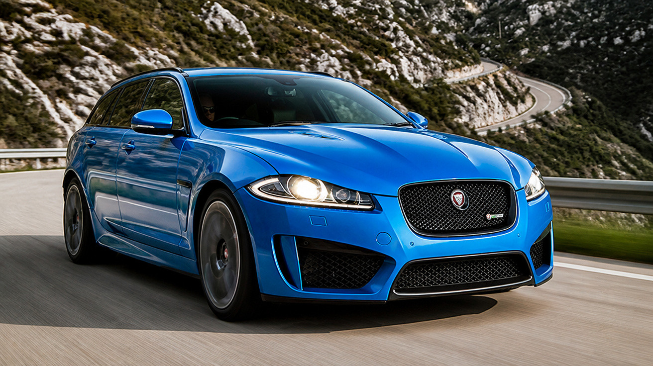 Carro esportivo azul da Jaguar dirigindo em estrada sinuosa próxima a montanhas rochosas.