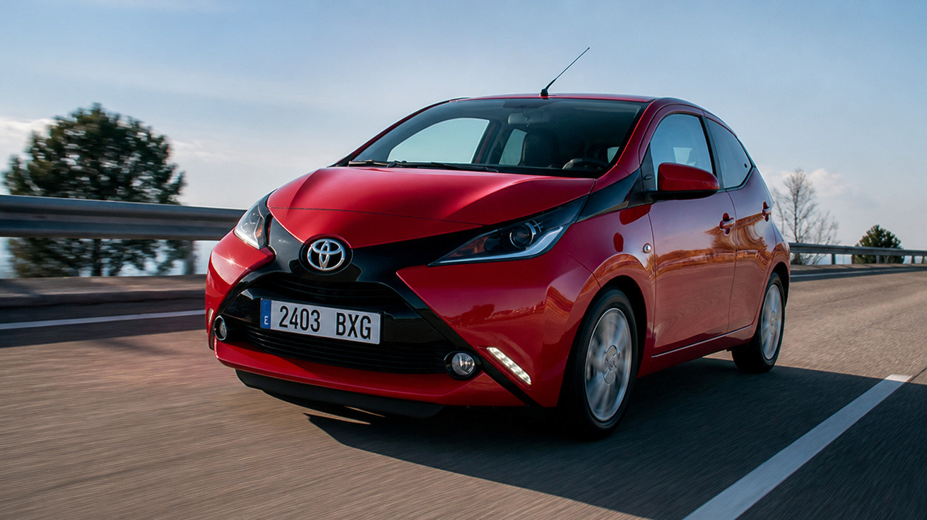 Carro vermelho Toyota em movimento na estrada sob céu azul claro.