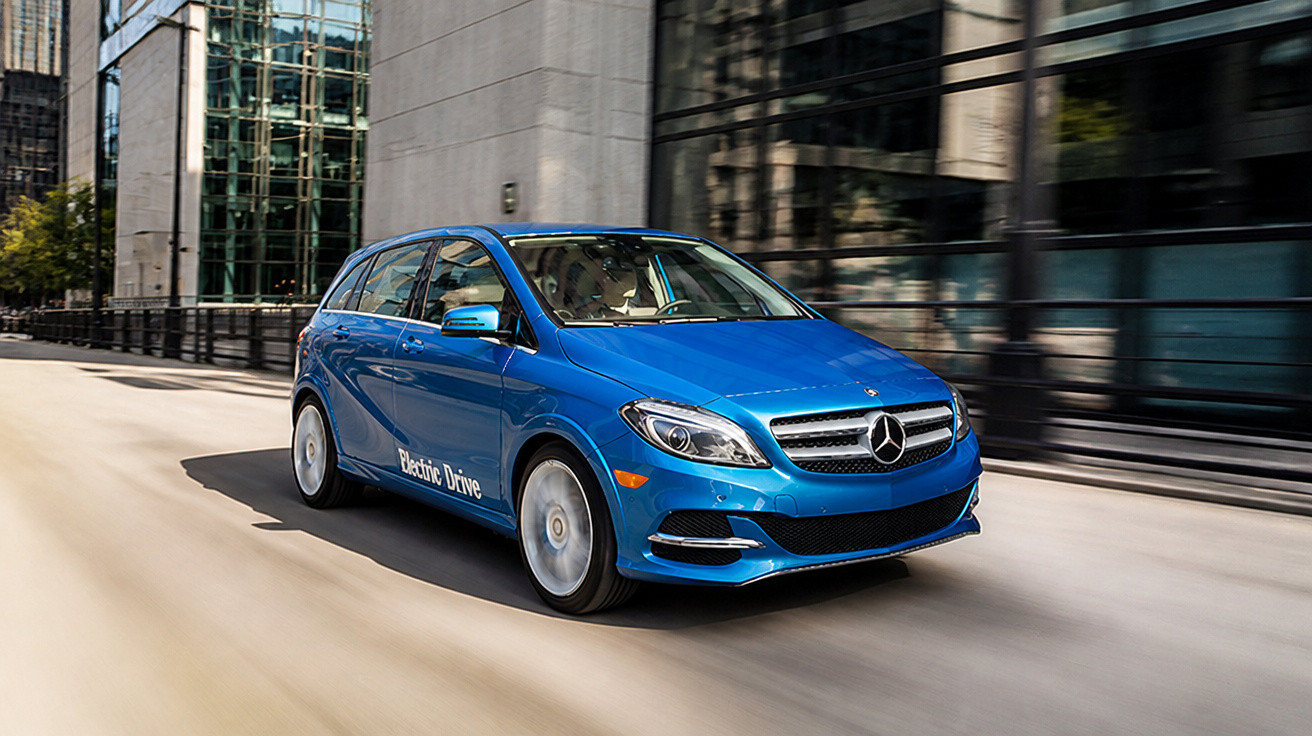 Carro elétrico azul Mercedes-Benz em movimento, em área urbana com prédios de vidro ao fundo.