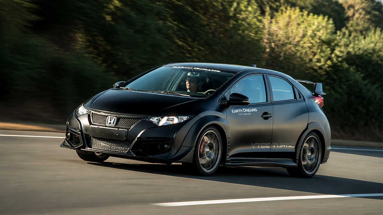 Carro Honda preto esportivo em movimento, conduzido por homem, em estrada com árvores ao fundo.