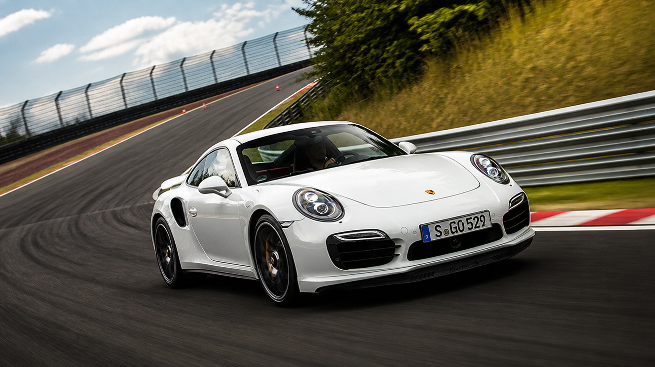 Carro esportivo branco Porsche 911 em alta velocidade em pista de corrida curvada.
